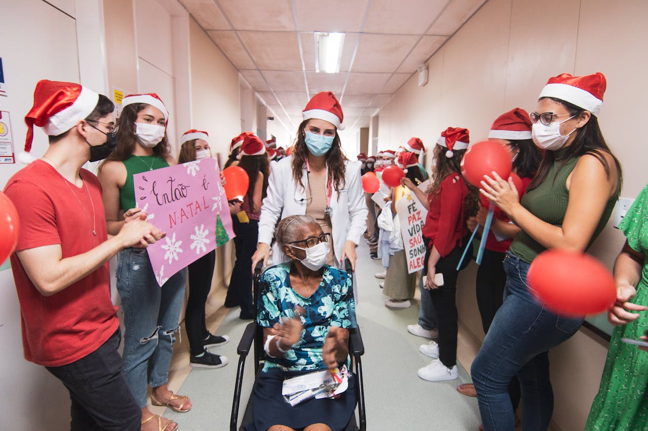A joyful Christmas celebration in a hospital corridor with staff and visitors in Santa hats supporting a patient.
